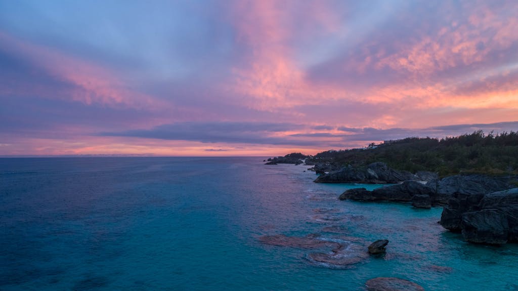 Captivating sunset over Bermuda's rocky coastline with vivid skies and tranquil sea.