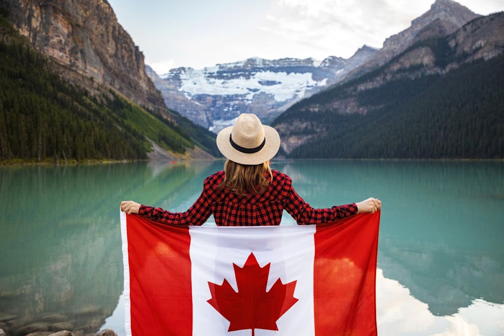 Woman holding a Canadian flag at stunning Lake Louise, Alberta, embracing nature and patriotism.