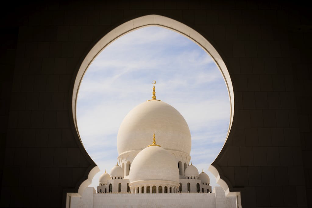 Captivating view of white domes of Sheikh Zayed Grand Mosque through an archway against the blue sky.