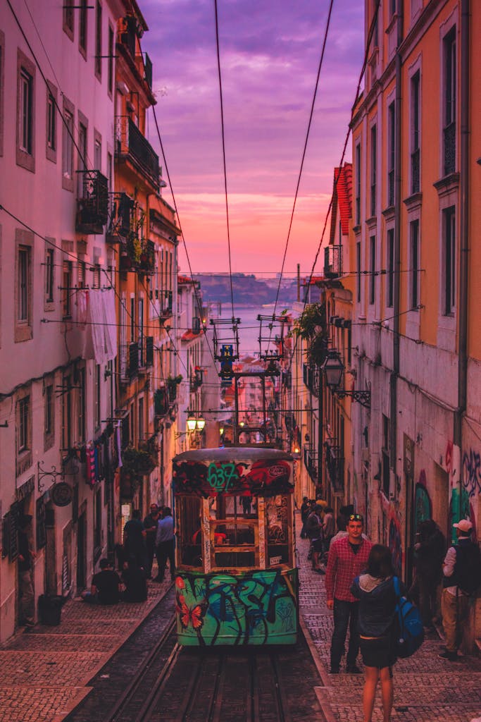 Colorful tram navigating a narrow street in Lisbon during sunset with people and architecture.