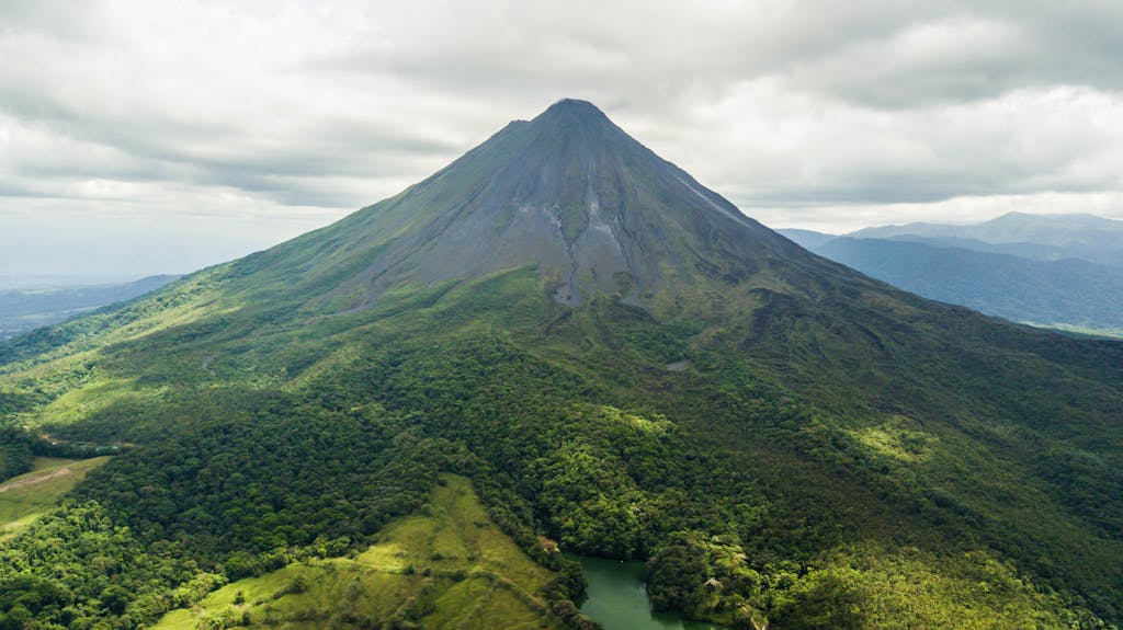 Dramatic aerial view of the lush green Arenal Volcano in Costa Rica against a cloudy sky.