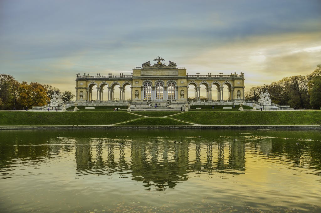 A stunning view of Schönbrunn Palace's Gloriette reflecting in a tranquil pond at sunset.